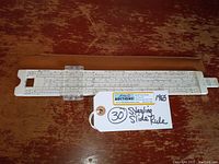 Full view of the 1965 Sterling slide rule on wooden surface with store tag showing '30' and label indicating year 1965.
