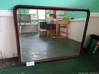 Full view of large rectangular antique mirror with rounded corners in dark wood frame placed against light green wall.