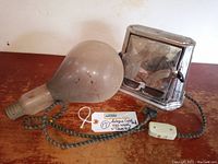 Photo showing the vintage Son Chief metal toaster and the large 750 watt light bulb side by side on a wooden surface with power cord visible.
