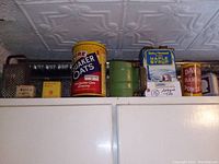 Shelf top view showing multiple vintage advertising tins including Quaker Oats, maple syrup, baking powder, mace, and ground mace tins, plus metal grater and flour sifter.