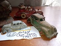 Four antique cast iron and diecast toys on wooden surface showing overall item condition and scale with handwritten lot number.