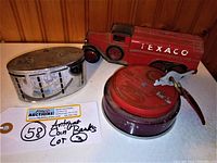 Photo showing three vintage metal coin banks placed together: the red Texaco truck bank, a round silver-colored bank, and a red round bank with a key attached.