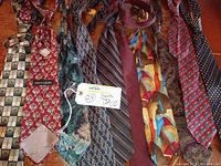 Photo showing the lot of 10 men's neckties arranged on a wooden surface, displaying different colors, patterns and fabrics including geometric, floral, striped and abstract designs along with a necktie knot accessory.