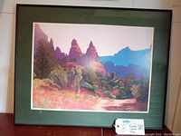 Framed colorful mountain print with green mat and thin black frame.