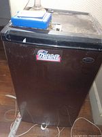 Front view of black Sanyo refrigerator with Patriots sticker on door, showing exterior condition and logo.