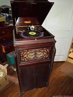 Full view of the antique Victrola with the lid open, showing the turntable and wood cabinet on wheels in a room with wooden floor.