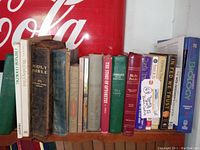 Side view of a shelf with multiple vintage books including several Holy Bibles, Chinese Cooking book, dictionary, biology textbook, and religious titles.