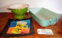 Photo showing the green enamel colander, enamel baking pan, and ceramic latte art plate together on a wooden surface.