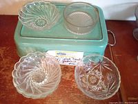 Five clear glass bowls of different sizes and patterns, including three Colonial Swirl pattern salad bowls and two additional serving bowls with starburst and ribbed designs. Bowls are placed on a vintage green metal tray.