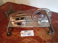 Side view of the metal deli slicer on a wooden table showing rust on the plate and the hand crank handle