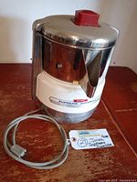 Front and side view of the juicer showing stainless steel body, red lift cap and power cord.