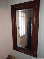 Full view of the tall rectangular mirror mounted on a wall showing its carved wooden frame and large reflective glass surface.