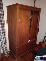 Front and side view of the mahogany wood armoire closet showing solid wood construction, sliding door partially open revealing interior hanging space