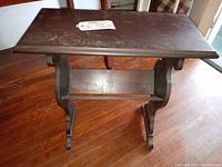 Side view of wood vintage side table showing V-shaped bookshelf underneath, curved legs, and wood finish with signs of wear.