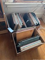 Three cardboard boxes filled with vinyl record albums in sleeves, showing various album spines and visible wear.