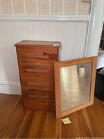 Photo showing antique wooden chest with four drawers and a detached wooden framed mirror leaning against it.