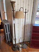 Photo showing two tall antique brass floor lamps with one having a beige fabric shade, and a smaller vintage table lamp in front.