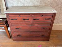 Front view of antique wooden dresser with white marble top, showing four drawers with metal handles and keyholes.