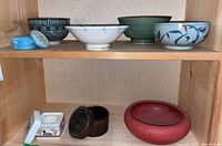 Shelf display of six ceramic bowls on top and two wooden boxes on bottom shelf showing color and design variations