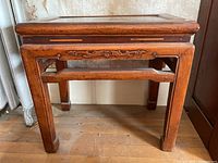 Front angle view of the small Asian wooden table with carved details and visible wear.