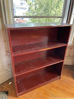 Front angled view showing entire bookshelf with three shelves, reddish-brown wood, dust and scratches visible