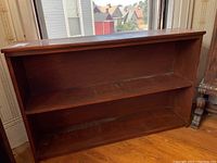 Front view of two-tier wooden bookcase showing shelves and surface wear.