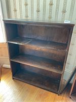 Front view of the three tiered wooden bookcase with visible wear on shelves and back panel.