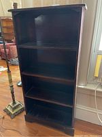 Wooden four tier bookcase shown from front with visible scratches and signs of wear on shelves and sides.