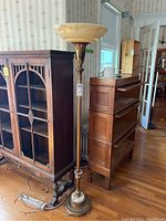 Full image of the tall brass and marble floor lamp standing next to wooden furniture, showing its overall height and silhouette.