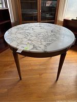 Full view of round marble top table with wooden base and tapered legs