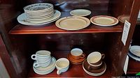 Shelving containing stacks of decorated and plain plates on top with cups and saucers below in various colors and designs.