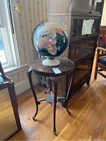 Side view of dark wooden circular side table with globe on top, showing table legs and condition