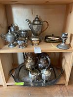 Shelf with multiple silver plated serving items including pitchers, jars, teapots, butter tray, and a weighted sterling candle holder.