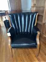 Front view of vintage armchair showing black vinyl channel back and wooden frame with nailhead trim.