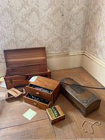 Five wooden keepsake and jewelry boxes arranged on wooden floor; one large box opened showing empty interior, a smaller box showing two drawers filled with paper clips, others closed.