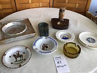 View of all eight ashtrays on a table showing variety in size, materials, and designs