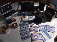 Wide view of lot showing multiple vintage cameras, lenses, filters, and Viewmaster with reels on table surface.