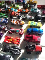 Photo showing multiple small die-cast toy cars in different styles and colors including red, blue, orange, green, silver, and black.