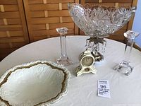 Photo of entire lot on table showing large crystal bowl compote with marble base, two crystal candlesticks, small vintage clock, and large decorative bowl