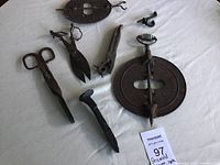 Photo shows the Griswold damper, ember tongs, scissors, spike, nail, and other fire tools laid out on white cloth, all with visible rust and wear.