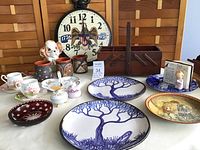 Photo of the entire lot showing Irish pottery plates, antique wooden sewing box, teacups, decorative bowls, and bicentennial clock.