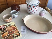 Photo showing all items including Le Creuset oval casserole dish, Disney cookie jar, Watt bean pot, three vintage soup mugs, sponge painted creamer, and cookbook.