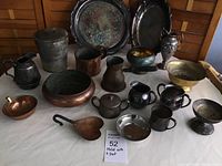 Full assortment of assorted vintage metal items displayed on white cloth including trays, bowls, pitchers, and a heart-shaped scoop.