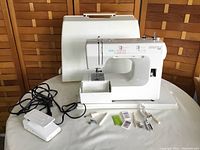 Full view of Kenmore 14 sewing machine with white hard carrying case behind, foot pedal, bobbins, presser feet, needles, and other accessories arranged in front