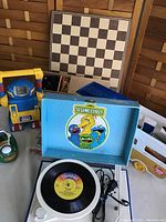 Photo of vintage toys including Talking Toby robot toy, Sesame Street record player with 45 RPM vinyl record, chessboard behind, Weebles camper and convertible car, Golden Tee golf set box.