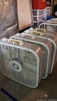 Four box fans lined up next to each other, showing front and top views with handles and controls visible.