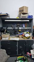 Front view of the Coleman/O'Sullivan workbench with pegboard hutch showing tools, boxes, and other items on the work surface and hanging on the pegboard. Locking drawers and cabinets below the work surface visible.