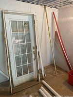 Full view of 32" white metal door with 15-lite glass panel leaning against wall, showing door hardware and adjacent trim pieces.