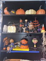 Shelf with assortment of Halloween figurines and faux pumpkins including pumpkin-headed figures, owl, Halloween tree, candy corn, and spider web decorations.