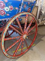 Side view of one painted wooden wheel showing red spokes with multicolor teardrop motifs.